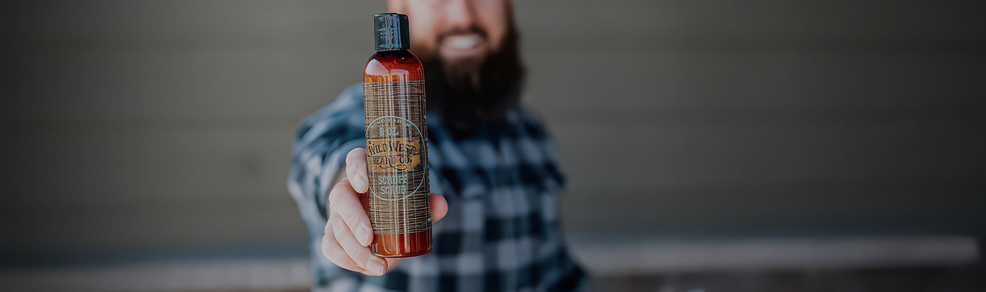 Person holding a bottle with a checkered shirt against a blurred background