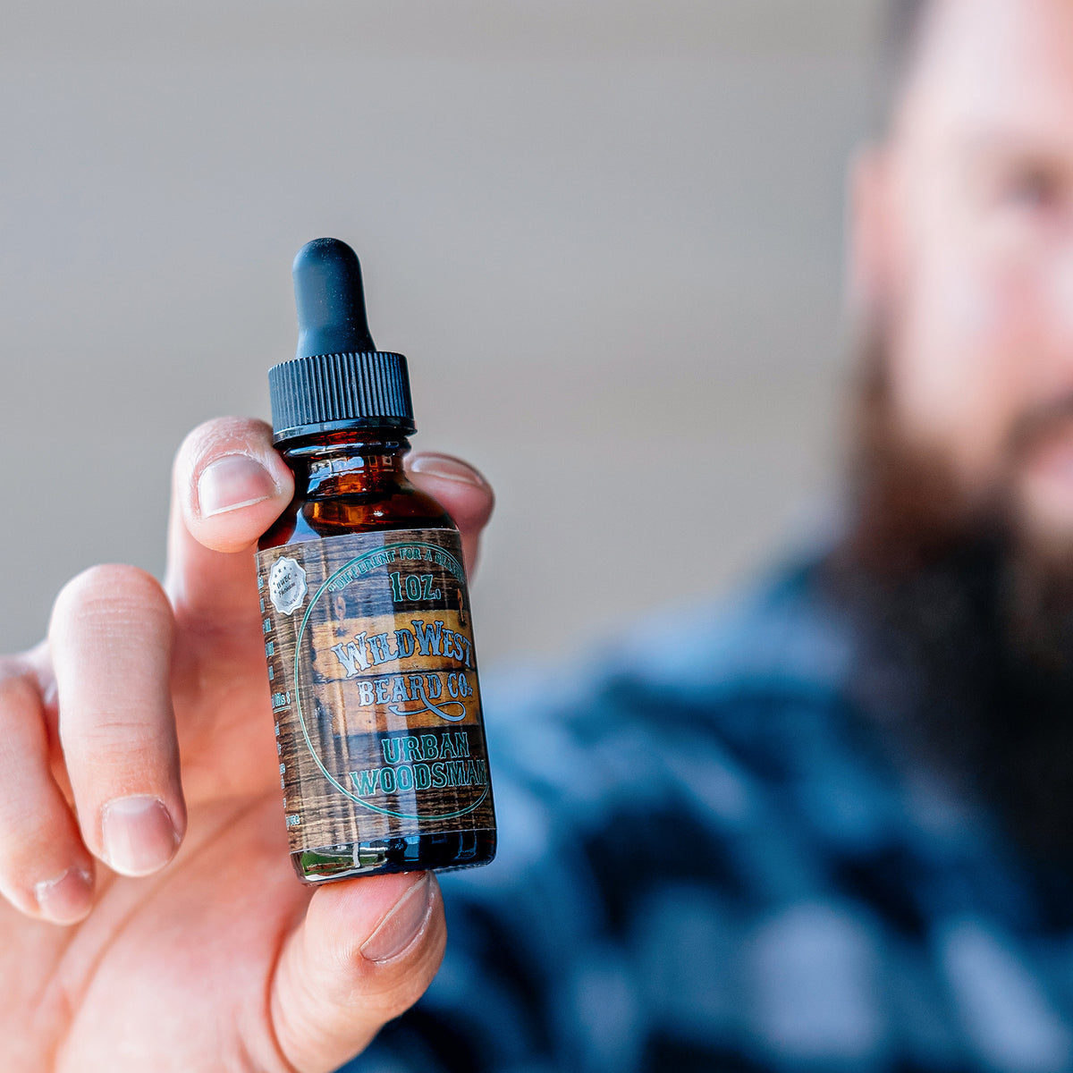 Hand holding a bottle of 'Wild West Beard Co.' beard oil with a blurred background